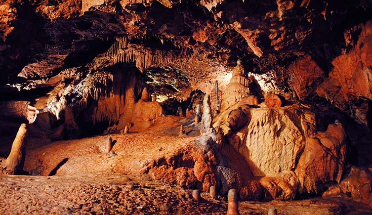 Stalacmites and stalactites emerge from the orange rock of Kent's Cave.