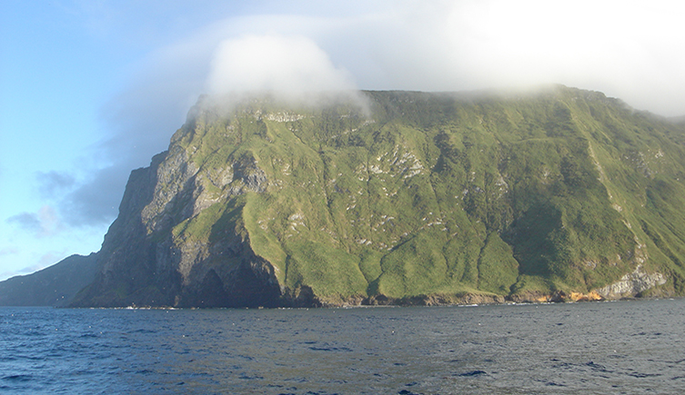 A island rising out of the water with cloud at the top of the green island cliff