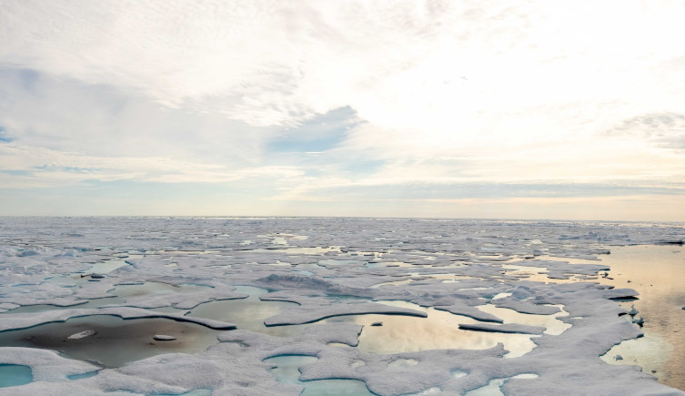 A view of sea ice in the bright sun with a cloudy sky above.