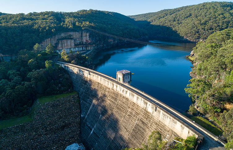Water is held back by a huge wall creating a large lake, surrounded by tree-covered hills