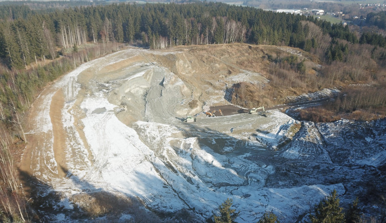 An aerial photograph of a clay pit surrounded by trees with digging equipment at the base.