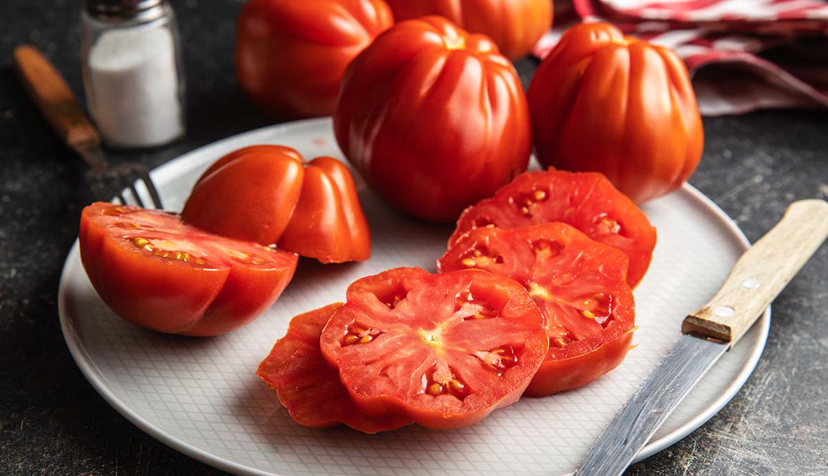 Beef tomatoes on a plate, with a pile of slices showing the inside.