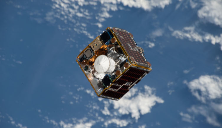 A cube-shaped satellite orbits above Earth