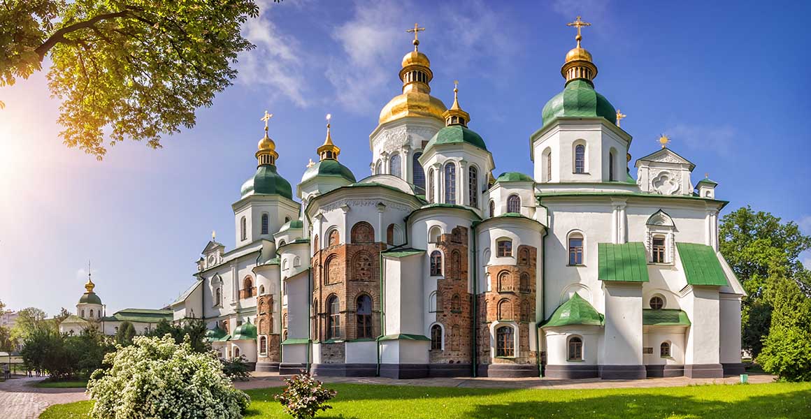 A picture of Saint Sophia Cathedral, showing its numerous golden and green domes and white exterior. 