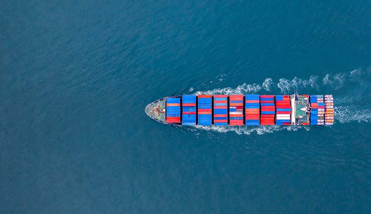 Seen from above, a cargo ship covered in colourful containers sails across the sea.