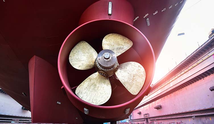 The bronze propeller of a large red ship. 