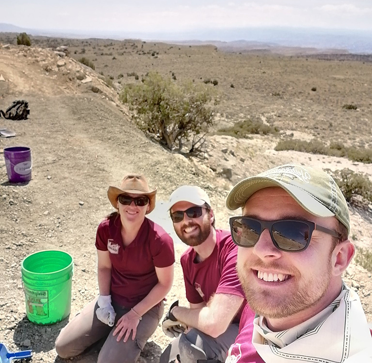 Three people taking a selfie in the desert with a bucket for digging fossils