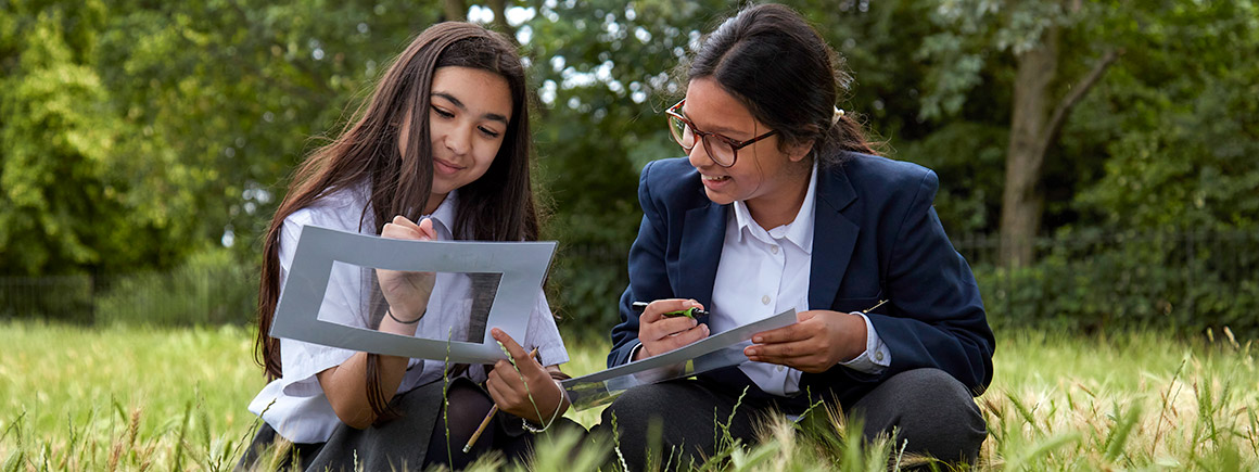 Two school children  in a park studying and documenting nature