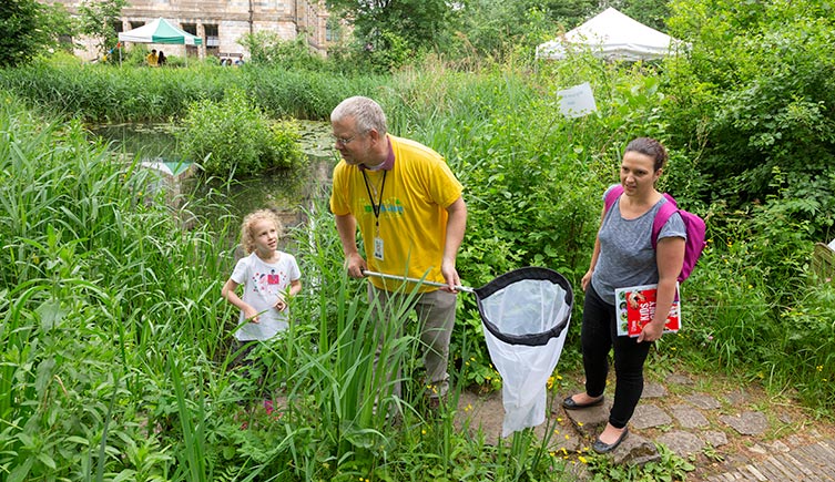 A scientist with a net helps a mother and daughter sweep for insects in the Museum's Wildlife Garden