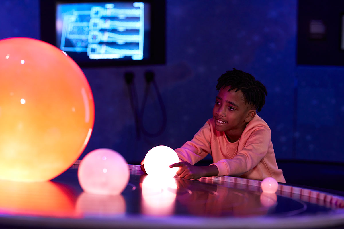 A photograph of a child holding a light up sphere representing a planet in our Space exhibition
