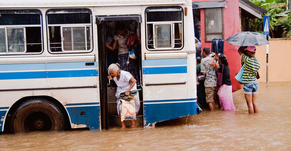 A woman steps off a bus onto a flooded Sri Lankan street