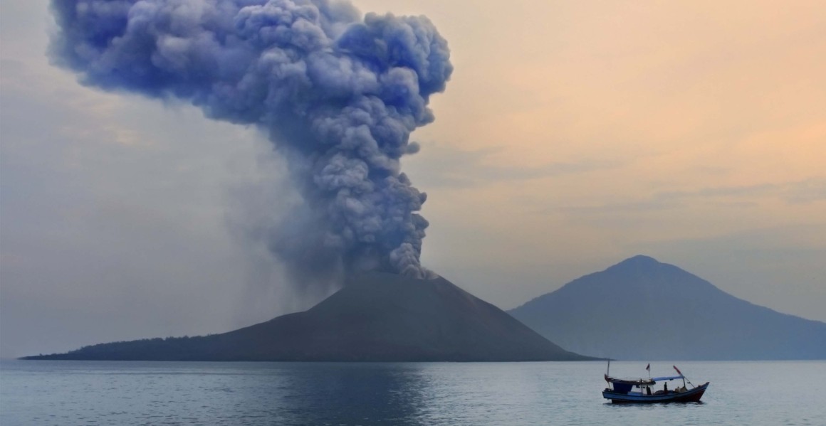 A boat glides over the water as Anak Krakatau erupts