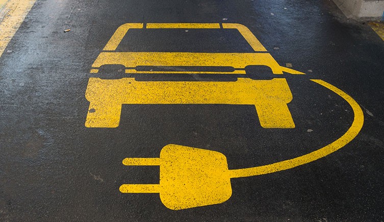 Logo featuring a yellow car, power cable and socket painted onto tarmac