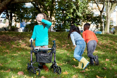 Three children play in a park. One child is covering their eyes and the other two are running away