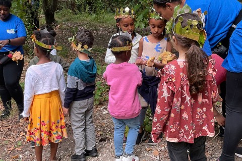 A group of children stand around with small, gold crowns and looking at a string with leaves threaded on it
