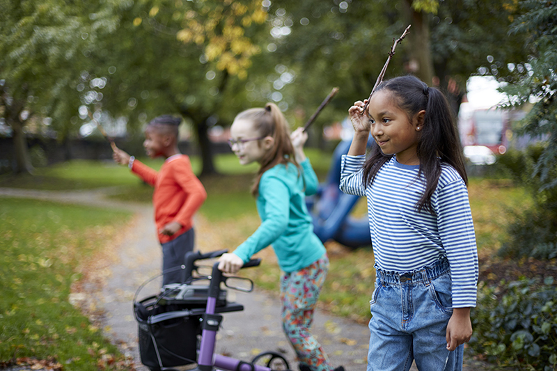 Three children crouch down in a line holding sticks.
